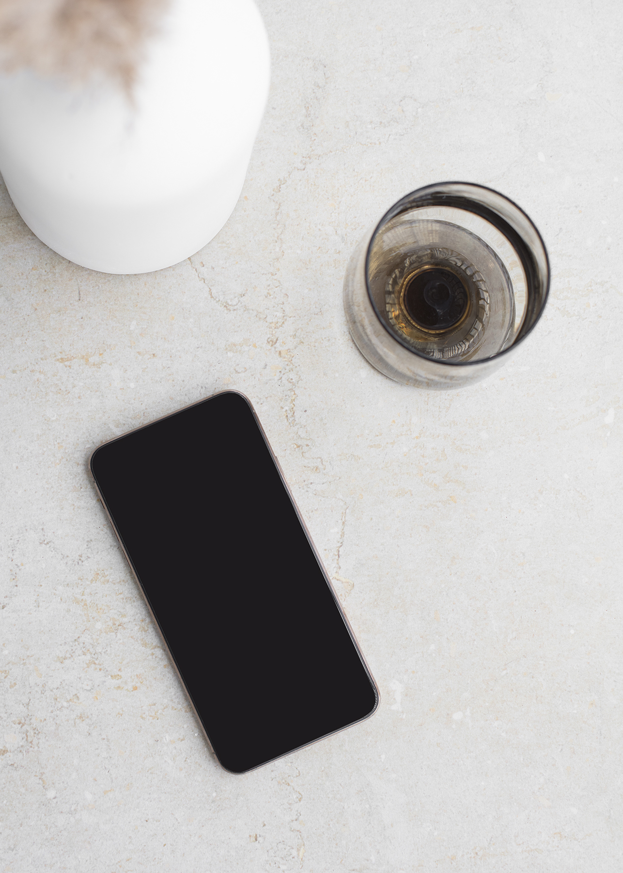 Styled flat-lay photo with a smartphone, glass cup, and white vessel on a light stone surface