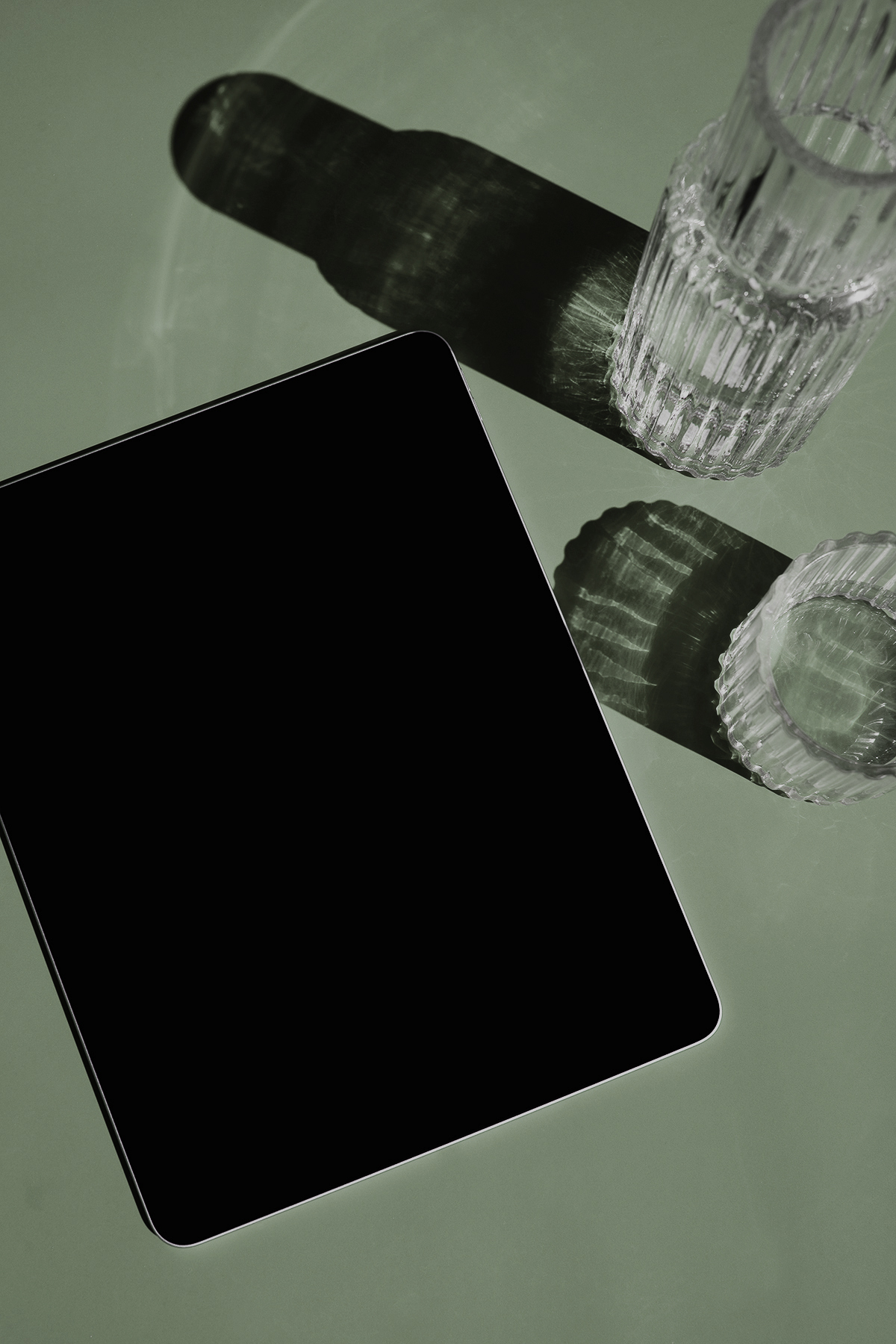 Black smartphone on a muted green surface with clear glass vessels