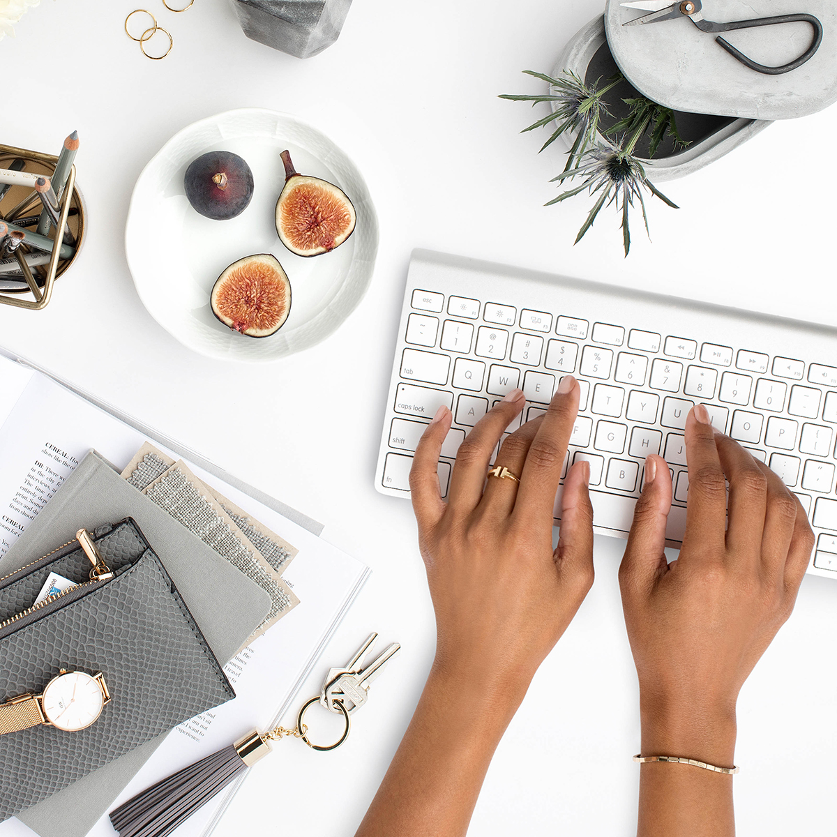 Top-down desk scene with keyboard, hands typing, figs, and styling accessories