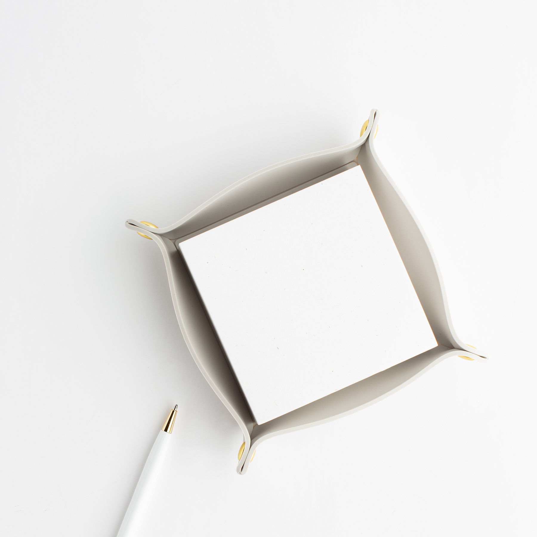 White notepad in a cream tray with gold accents and a white pen on a light background