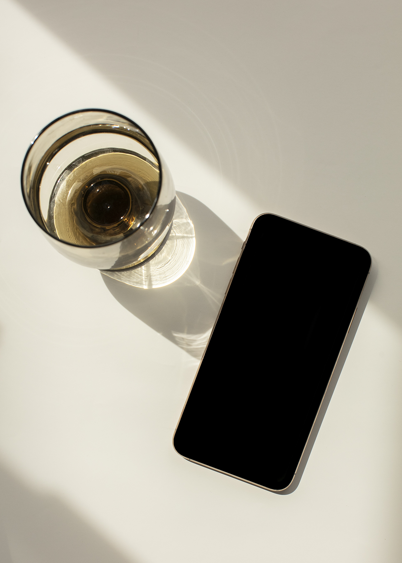 Glass with amber drink beside a smartphone on a light surface