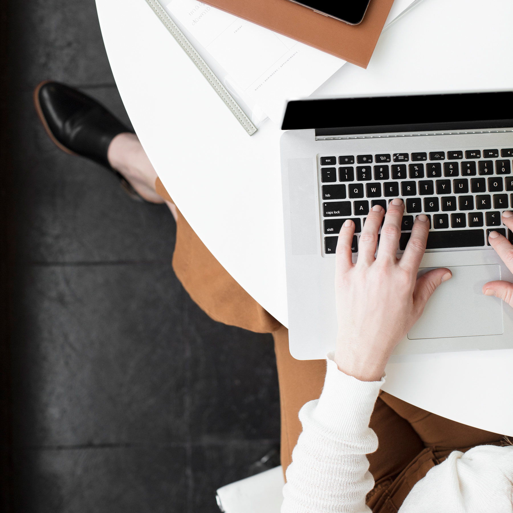 Person typing on a laptop at a white desk with notebook and phone
